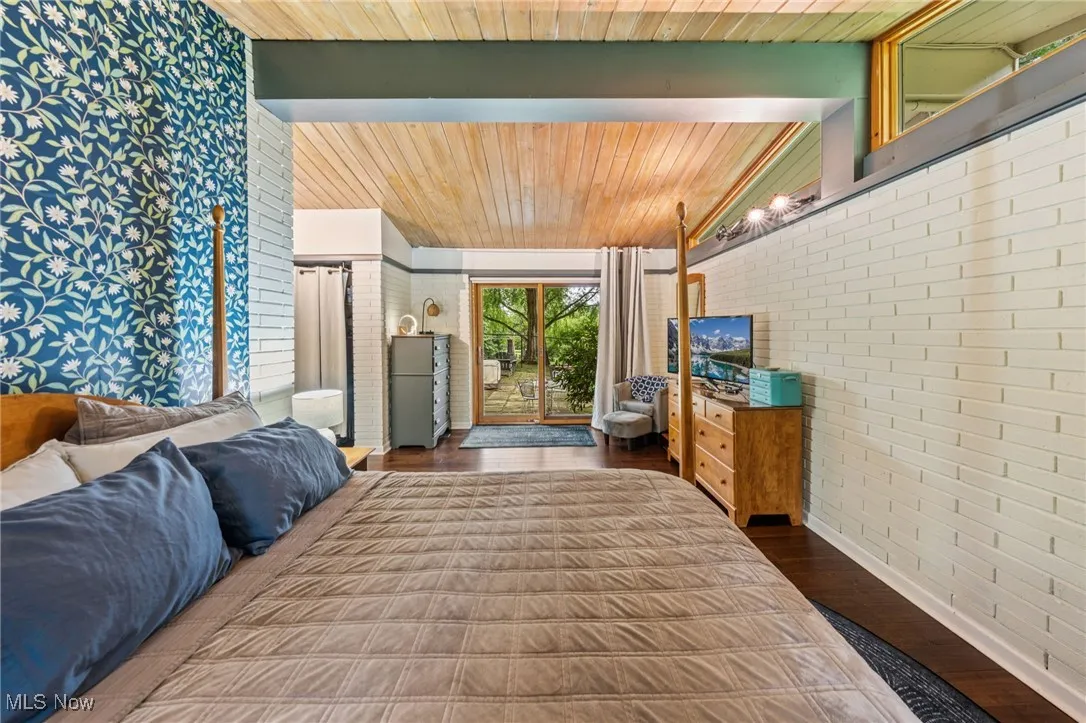 Bedroom with dark wood-style flooring, brick wall, wooden ceiling, and access to outside