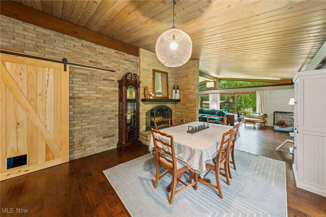 Dining space with a fireplace, a barn door, dark wood-style floors, brick wall, and wooden ceiling