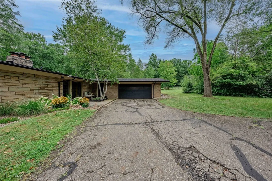 View of front of home featuring a garage, asphalt driveway, a front lawn, stone siding, and a chimney