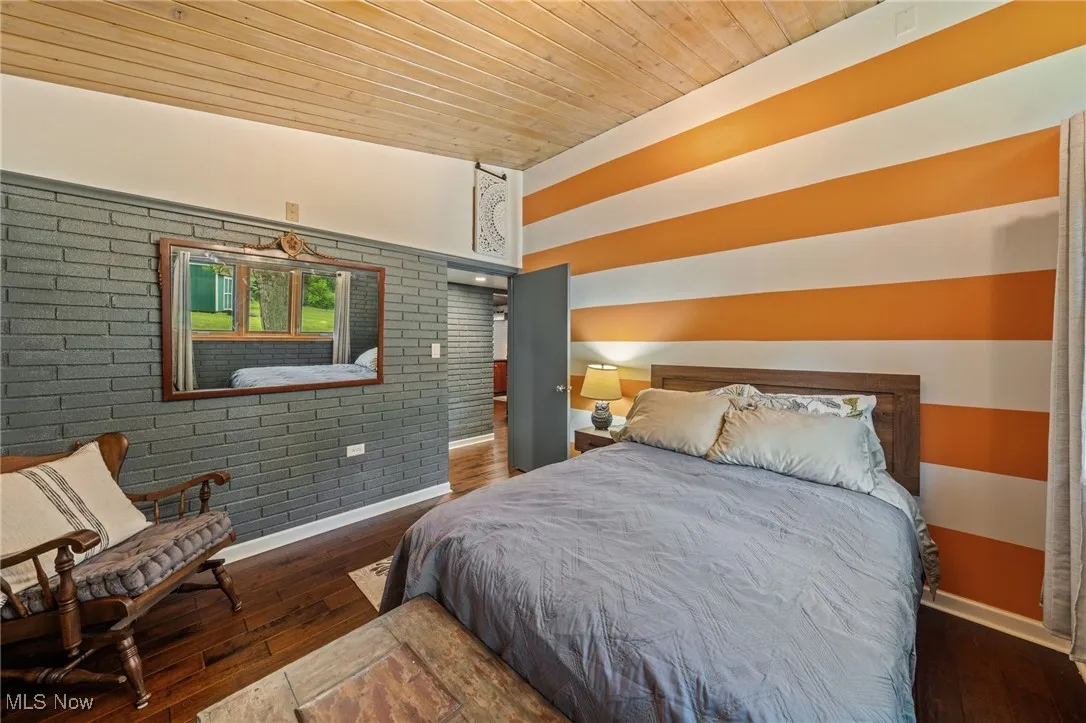 Bedroom featuring dark wood finished floors, wooden ceiling, and brick wall