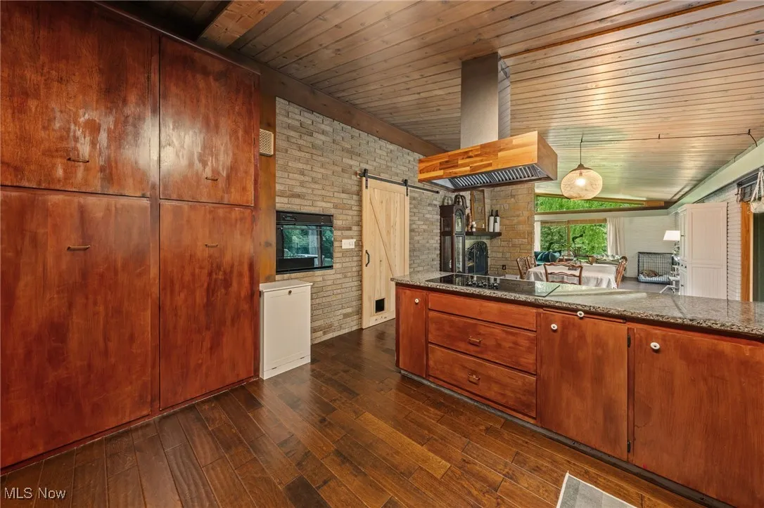 Kitchen with a barn door, brick wall, range hood, dark wood finished floors, and pendant lighting