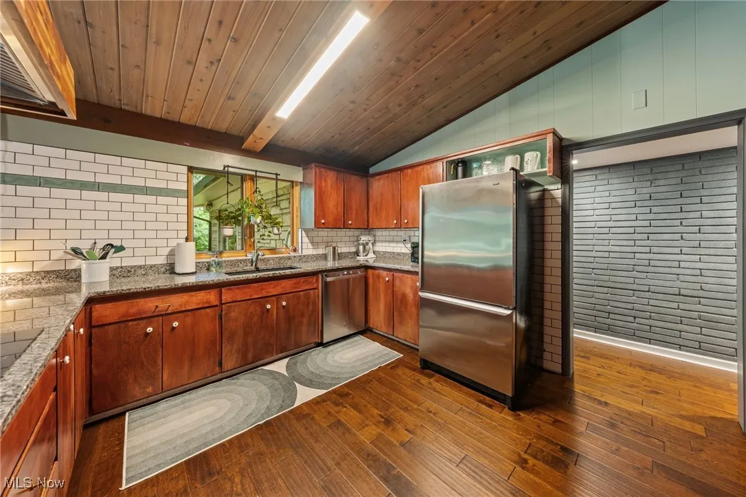 Kitchen with dark stone countertops, dark wood-type flooring, stainless steel appliances, extractor fan, and tasteful backsplash