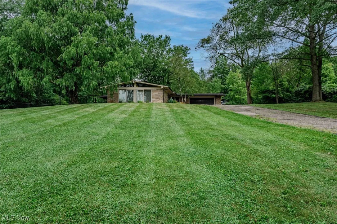 View of green lawn featuring dirt driveway and an attached garage