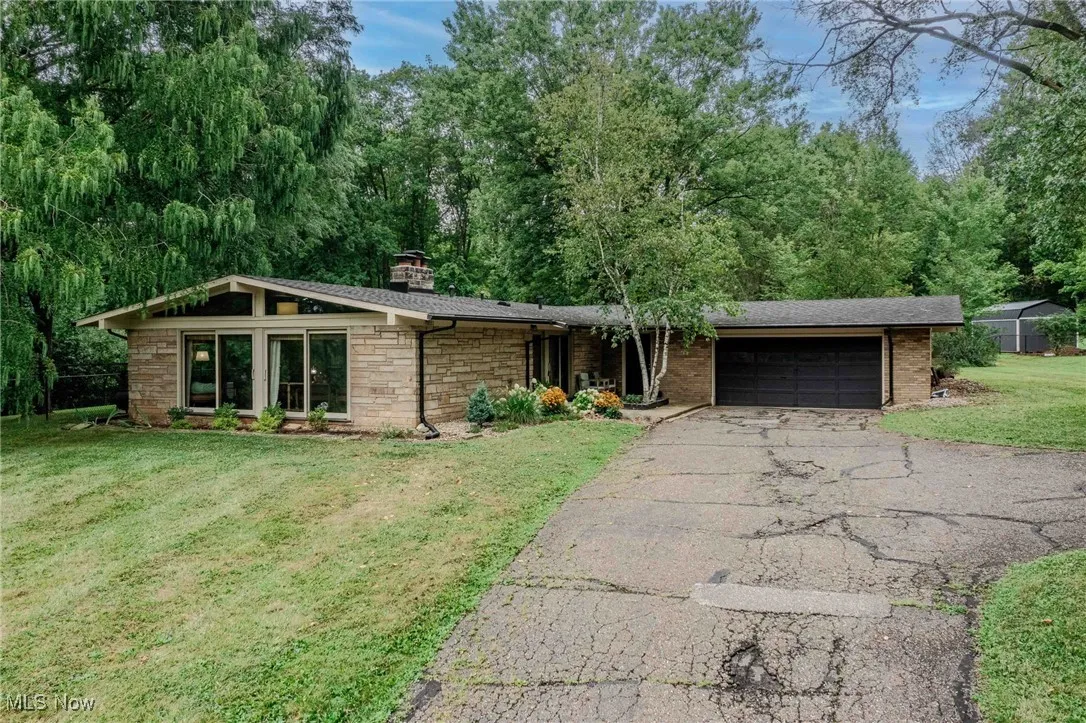 View of front facade featuring driveway, an attached garage, a front lawn, a chimney, and stone siding
