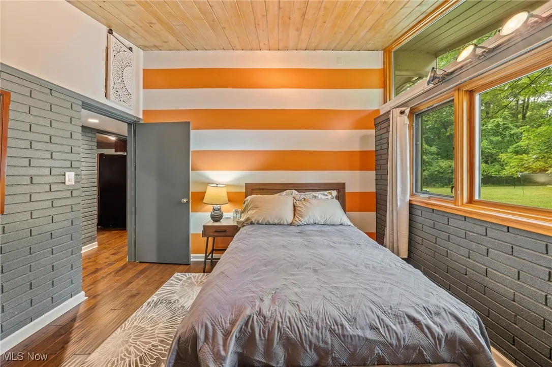 Bedroom with brick wall, wood finished floors, black fridge, and wooden ceiling