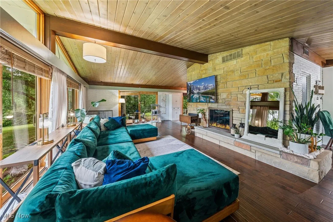 Living room with wooden ceiling, a stone fireplace, and hardwood / wood-style flooring