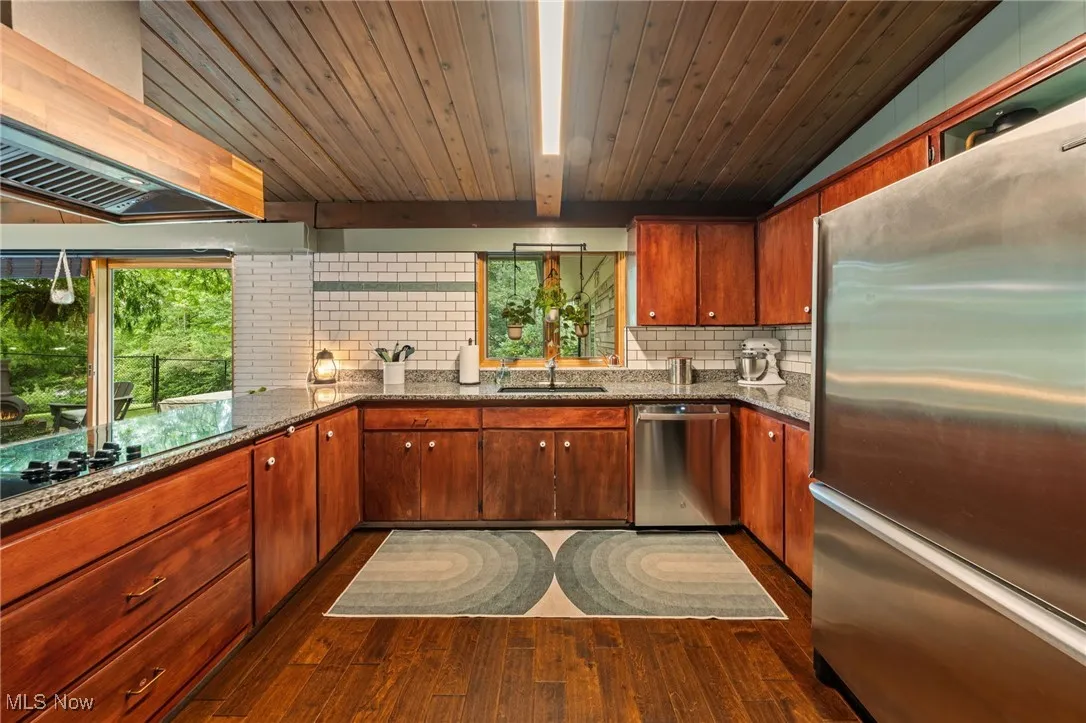 Kitchen with stainless steel appliances, dark stone counters, custom exhaust hood, tasteful backsplash, and dark wood finished floors