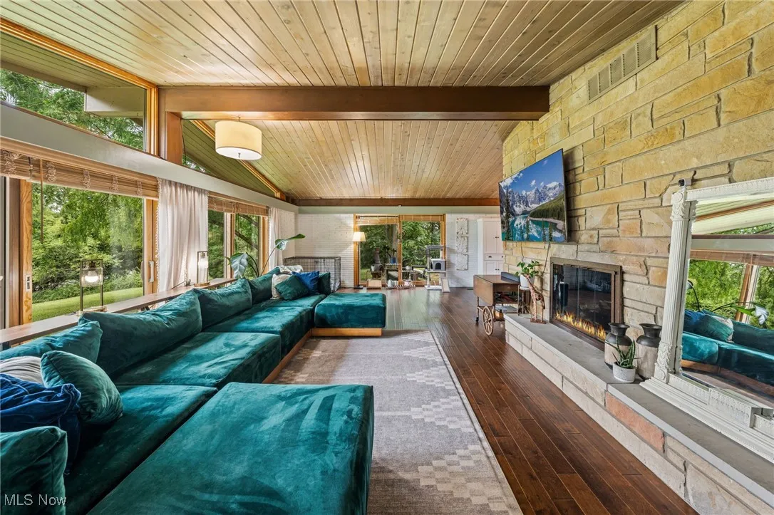 Living area featuring a stone fireplace, dark wood-type flooring, a wood ceiling with exposed beams, and high vaulted ceiling