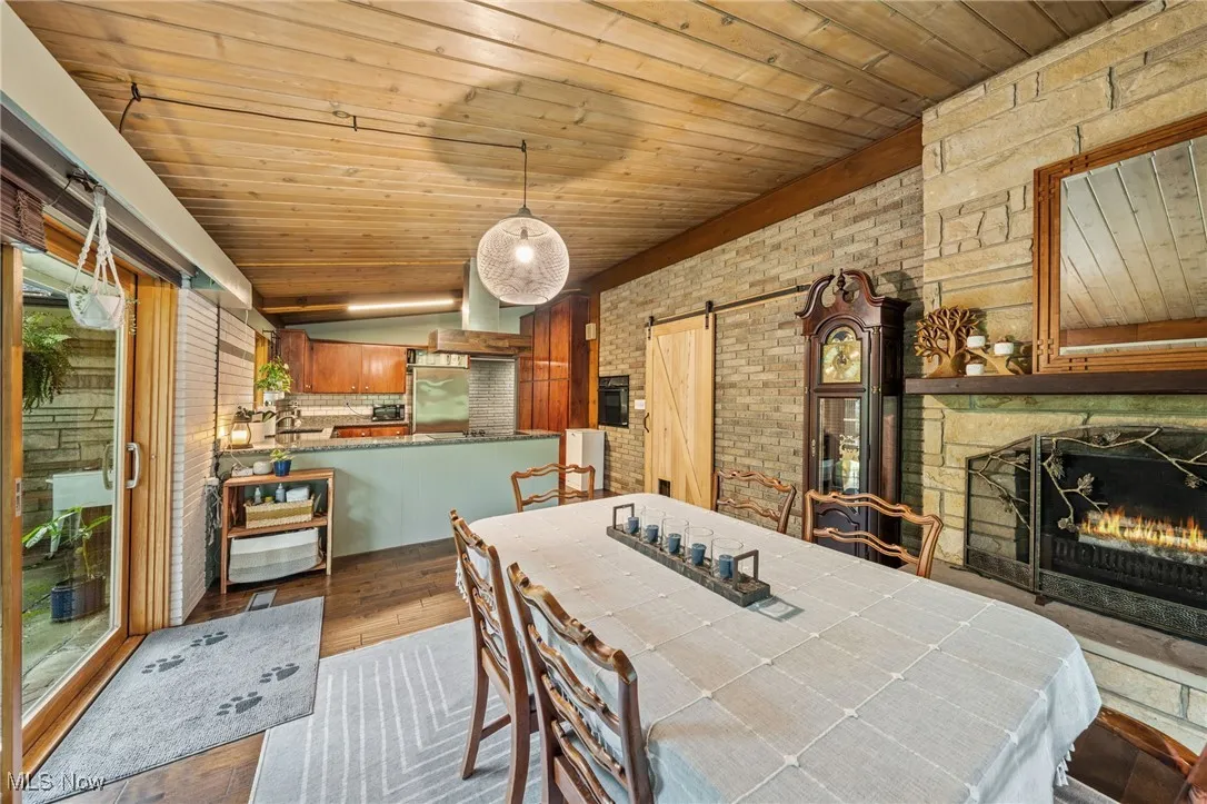 Dining room with a barn door, a stone fireplace, wood finished floors, lofted ceiling, and brick wall