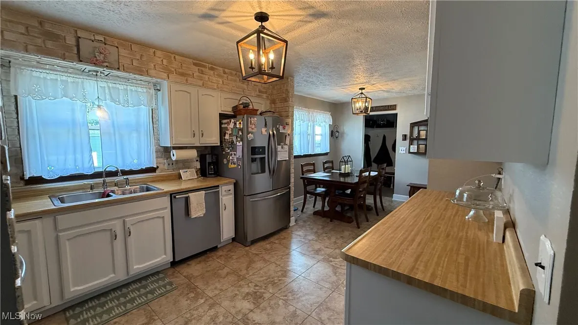 Kitchen featuring stainless steel appliances, white cabinets, hanging light fixtures, and light countertops