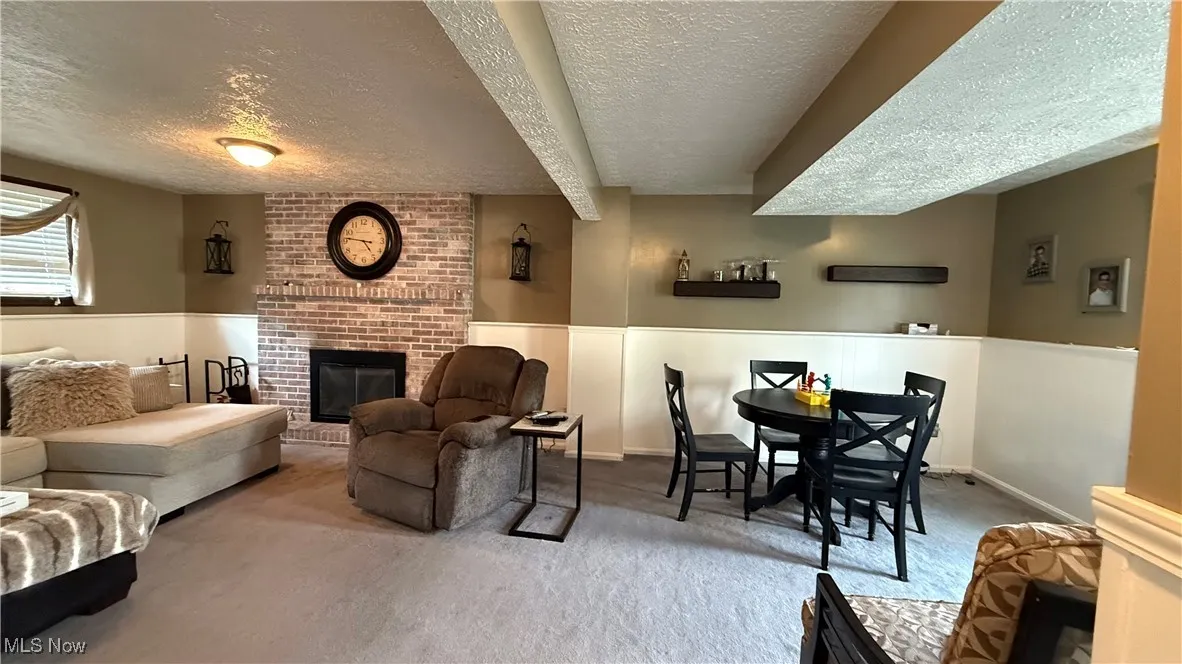Family room with a fireplace, a textured ceiling, carpet flooring, and a wainscoted wall