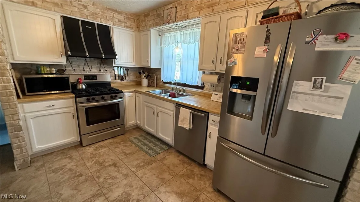 Large kitchen featuring stainless steel appliances, range hood, light countertops, tasteful backsplash, and white cabinetry
