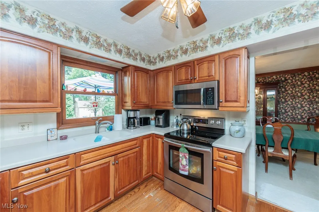 Kitchen with appliances with stainless steel finishes, light countertops, brown cabinetry, light wood-style flooring, and a textured ceiling