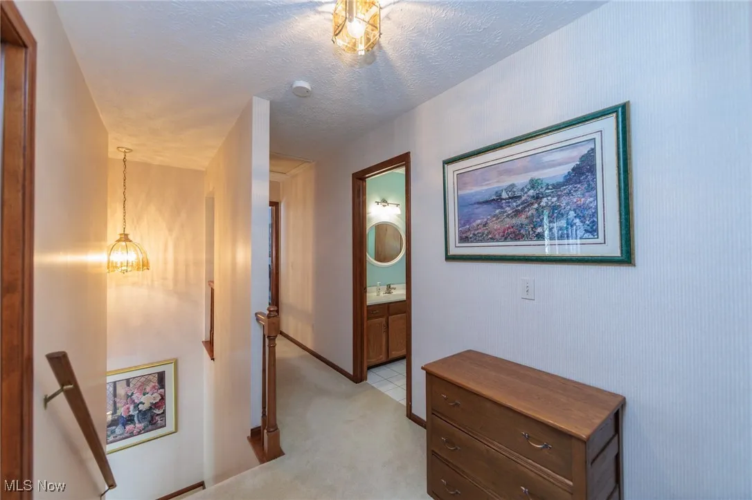 Hallway with an upstairs landing, light colored carpet, a chandelier, and a textured ceiling