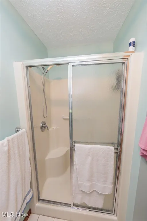 Full bathroom featuring a shower stall, a textured ceiling, and light tile patterned floors