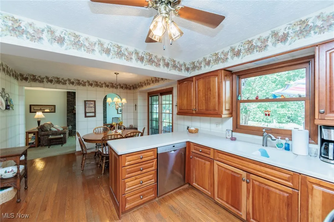 Kitchen with brown cabinets, a chandelier, stainless steel dishwasher, light wood-style floors, and hanging light fixtures