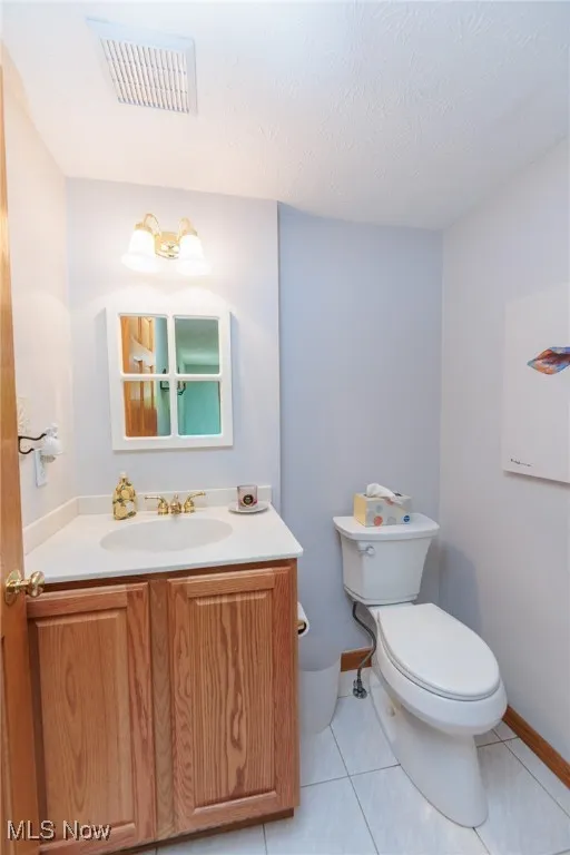 First floor half bathroom with vanity, light tile patterned flooring, and a textured ceiling