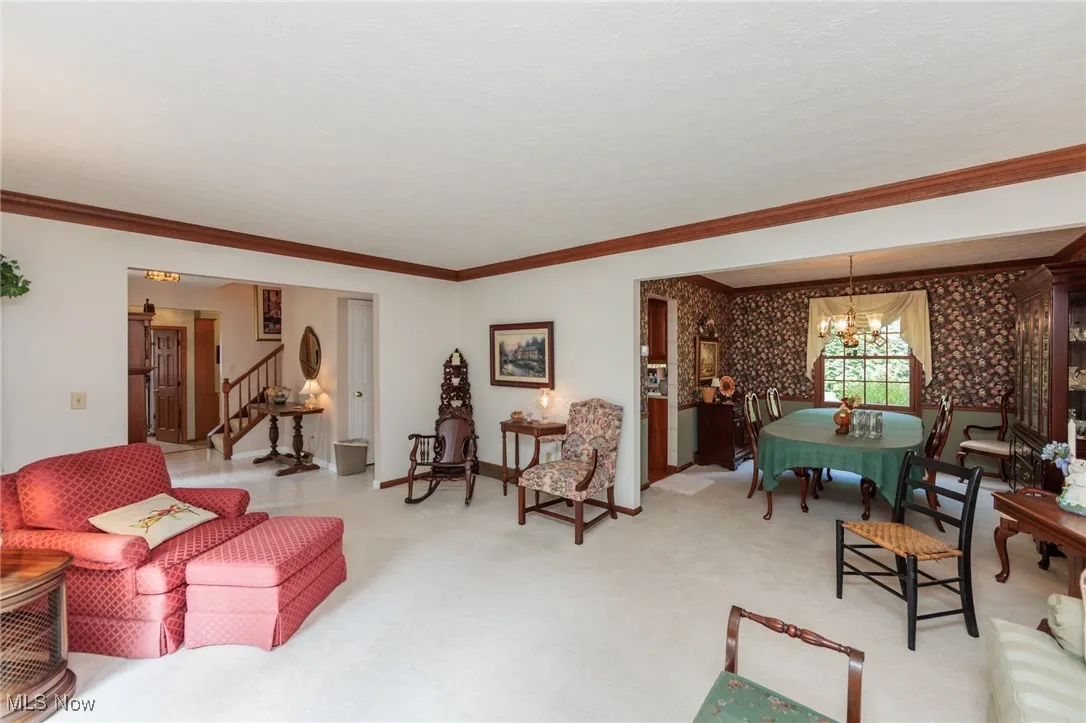 Living area with ornamental molding, a chandelier, carpet, wallpapered walls, and stairs