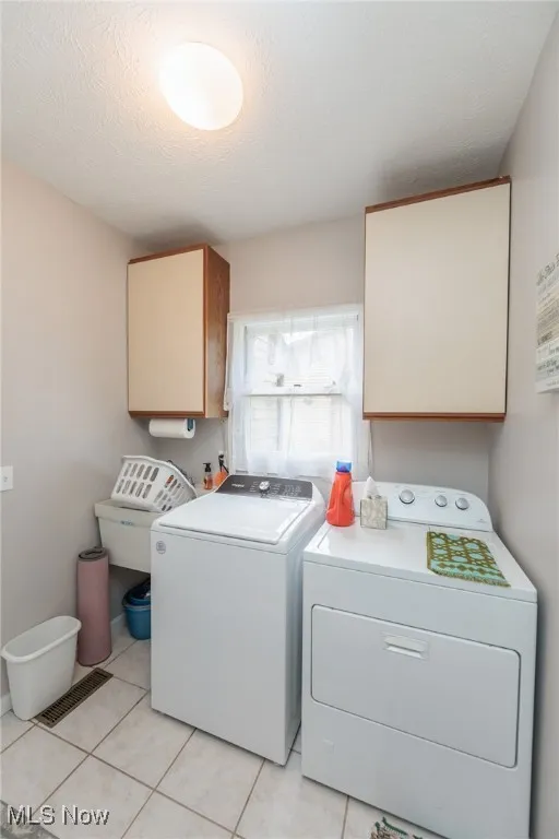 First floor laundry area featuring cabinet space, a textured ceiling, light tile patterned floors, and independent washer and dryer