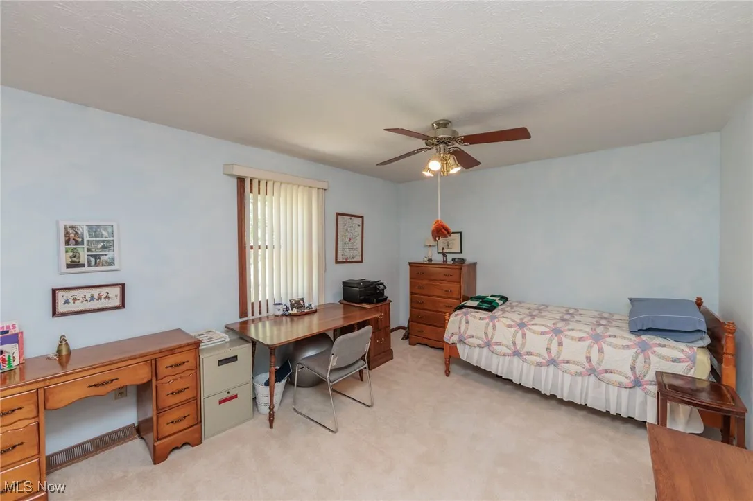 Bedroom with light carpet, an office area, ceiling fan, and a textured ceiling