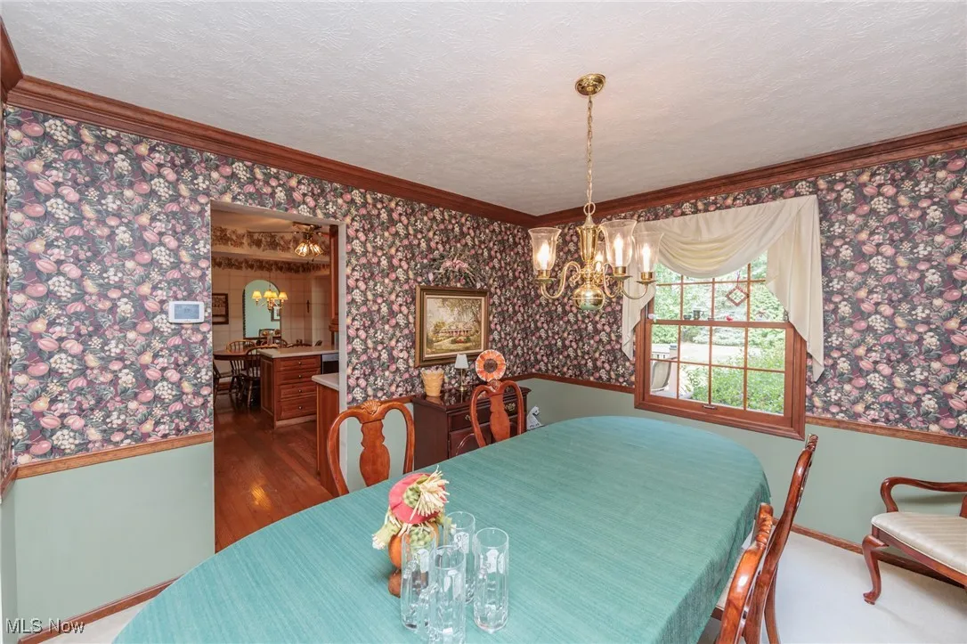 Dining room featuring wallpapered walls, a chandelier, ornamental molding, a textured ceiling, and wood finished floors