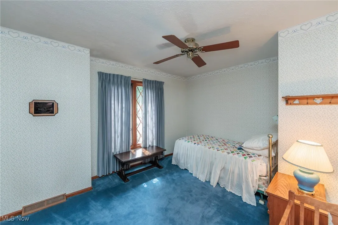 Carpeted bedroom featuring wallpapered walls, ceiling fan, and a textured ceiling