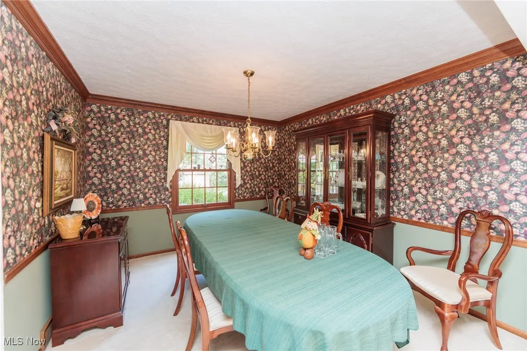 Dining space with wallpapered walls, a wainscoted wall, ornamental molding, a chandelier, and a textured ceiling