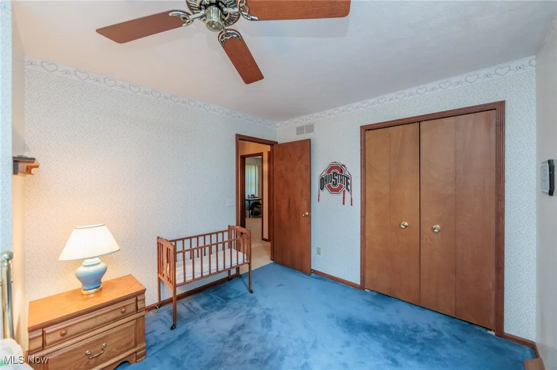 Bedroom featuring wallpapered walls, a closet, carpet flooring, ceiling fan, and a crib