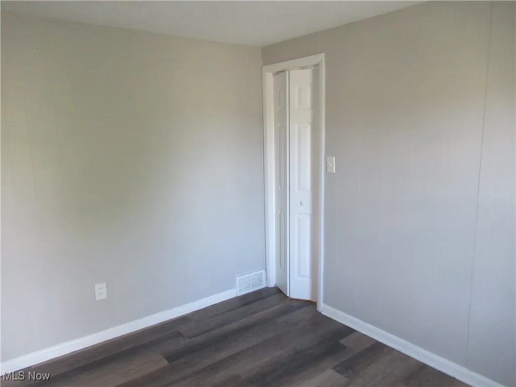 Spare room featuring dark wood-type flooring and baseboards