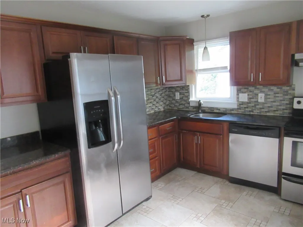 Kitchen with stainless steel appliances, backsplash, decorative light fixtures, dark stone countertops, and brown cabinetry
