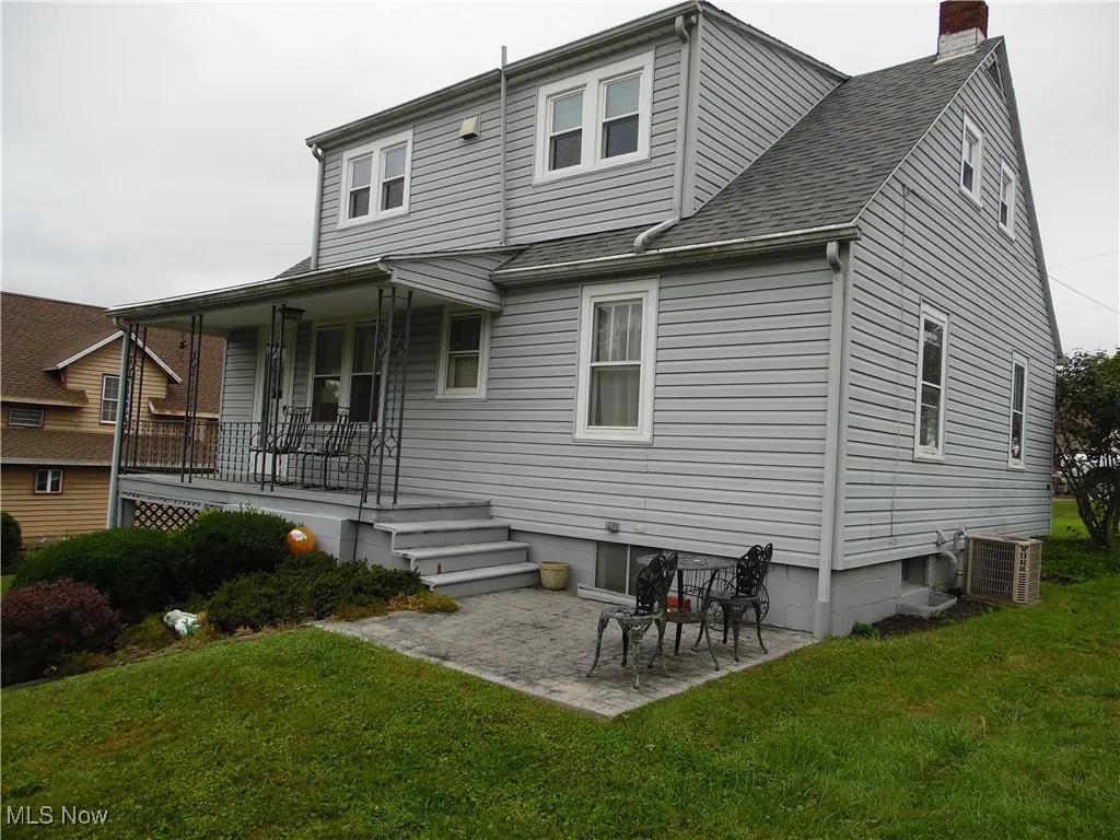 Rear view of house with a chimney, a patio area, a yard, roof with shingles, and covered porch