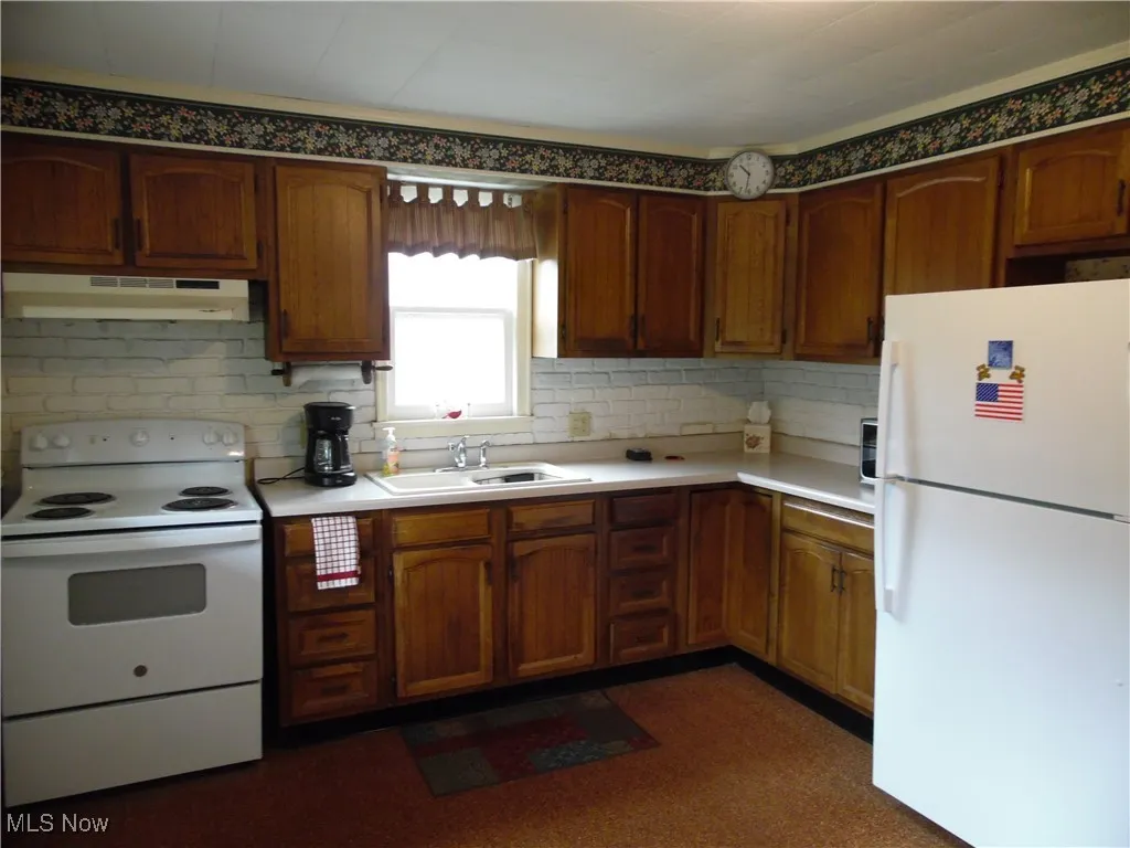 Kitchen with white appliances, light countertops, under cabinet range hood, and brown cabinets