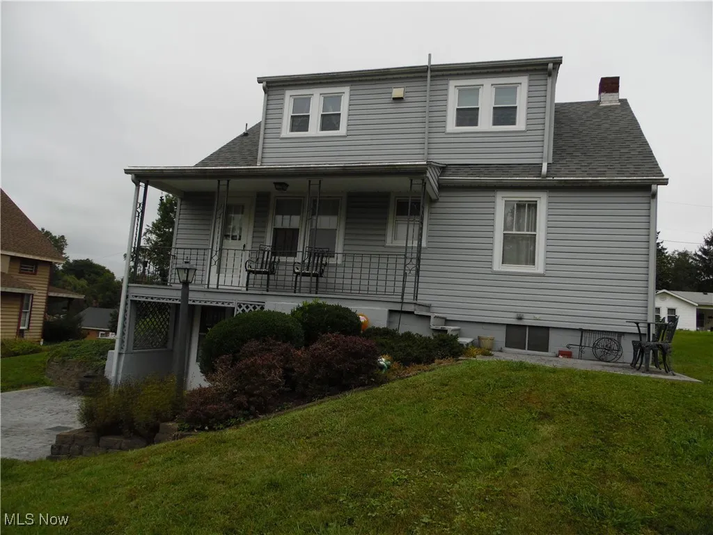 Back of property featuring a porch, a chimney, roof with shingles, and a yard