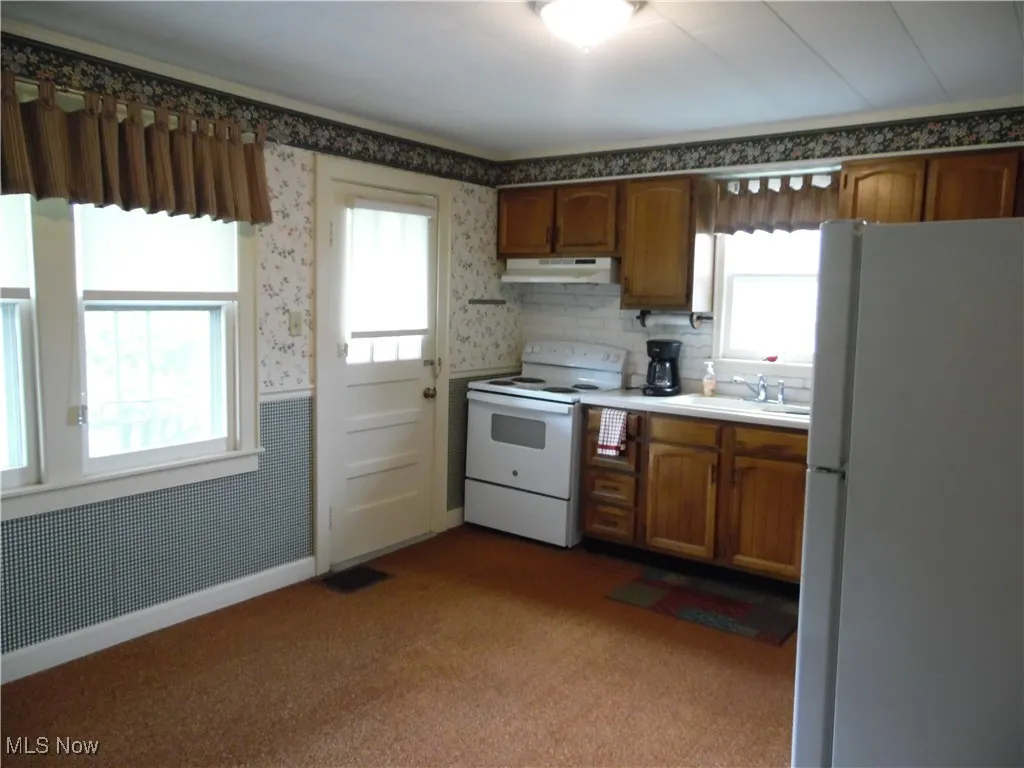 Kitchen with wallpapered walls, brown cabinets, white appliances, a wainscoted wall, and light countertops
