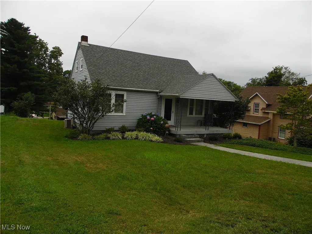 View of front of property featuring a front lawn, a chimney, and roof with shingles
