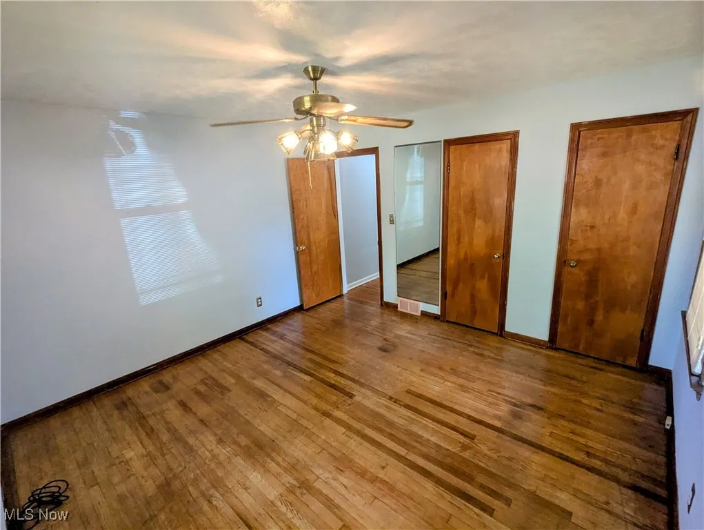 Another view of the second first floor Bedroom featuring, a ceiling fan, hardwood flooring, and his and her closets