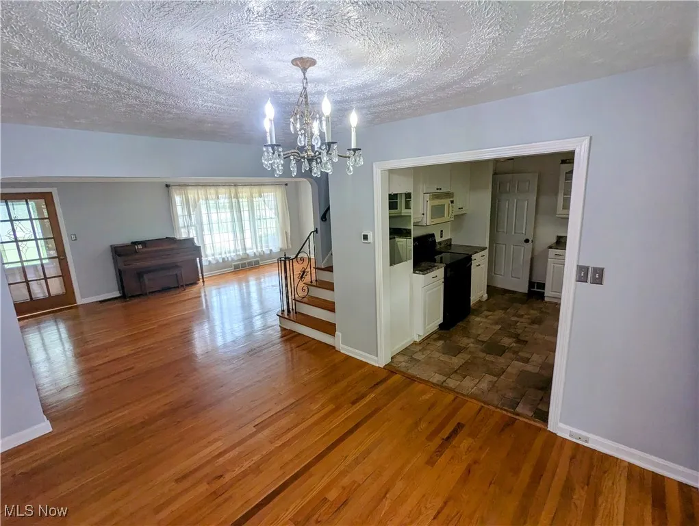 Dining area featuring a textured ceiling, and a chandelier, light hardwood floors opening to kitchen and four-season room