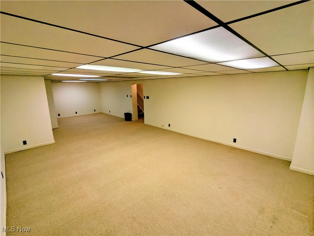 Finished below grade area featuring light colored carpet, stairway, and a drop ceiling