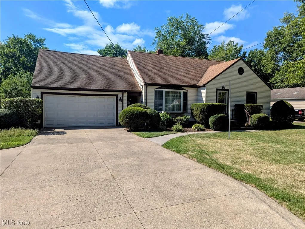 View of front of Cape Cod style home with an attached garage, and a deep front lawn