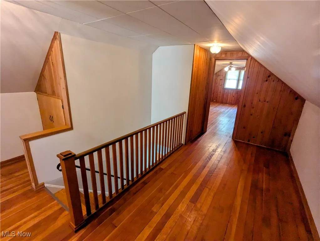 Second floor hallway with storage,  featuring hardwood flooring, lofted ceiling, and wooden walls