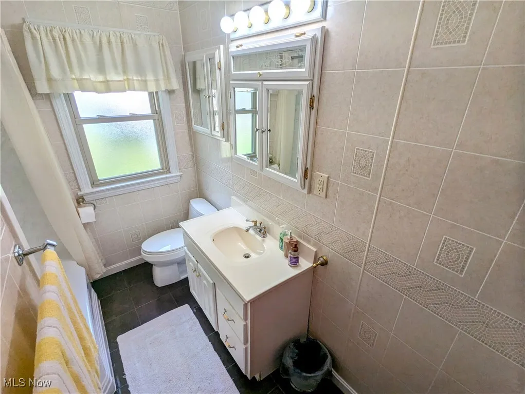 Full bathroom featuring tile walls, vanity, and dark tile patterned flooring