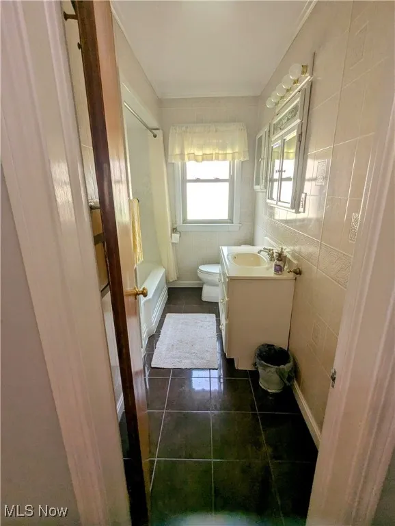 Bathroom with tile walls, dark tile patterned floors, vanity, and tub / shower combination