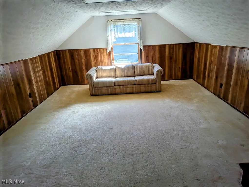 Additional second floor bedroom with wooden walls, a textured ceiling, carpet floors, lofted ceiling