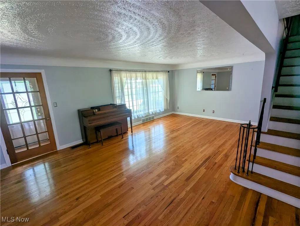 Another view of the living room featuring a bay window with window seat, a textured ceiling, stairs, hardwood floors, and healthy amount of natural light