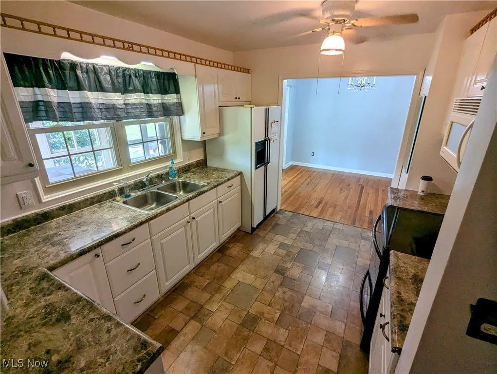 Kitchen featuring white cabinetry, white refrigerator with ice dispenser, black glass top electric stove, and ceiling fan
