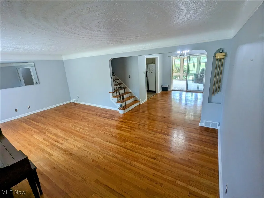 Living room featuring a textured ceiling, arched walkways, stairs, and light hardwood flooring