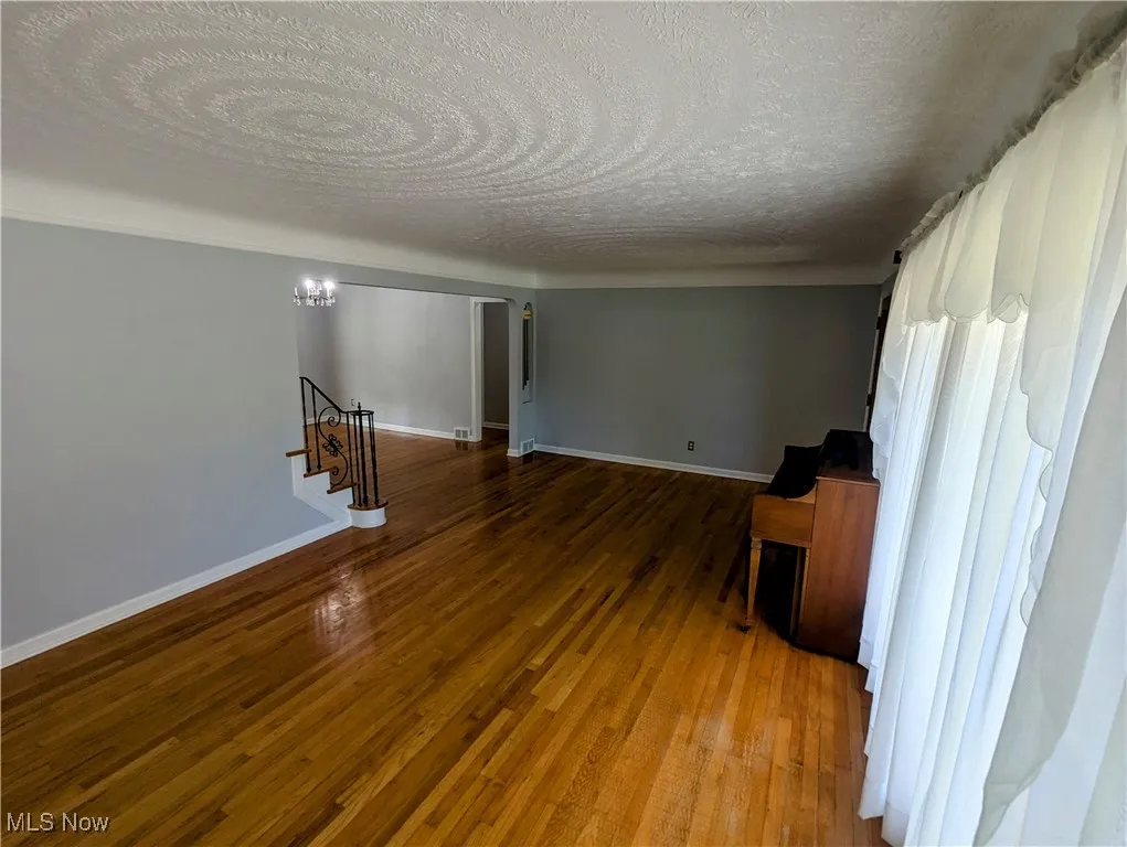Another view of the living room featuring a textured ceiling, stairs, hardwood floors, and healthy amount of natural light