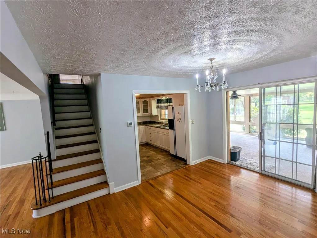 Dining area with light hardwood floors, stairway, a textured ceiling, and a chandelier