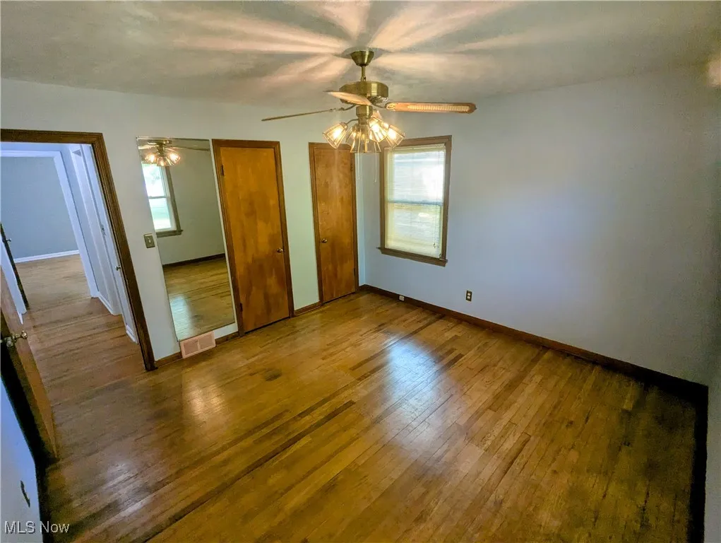 Another view of the second first floor Bedroom featuring, a ceiling fan, hardwood flooring, and his and her closets