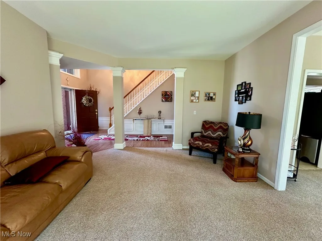 Carpeted living area featuring ornate columns and stairway